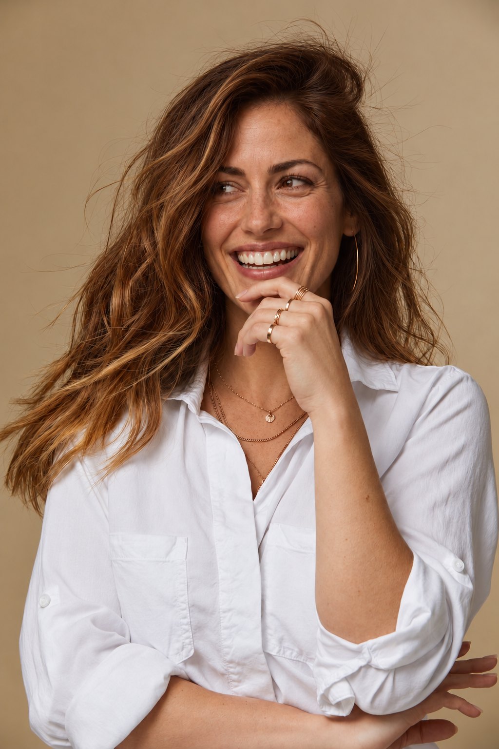 Woman in a white shirt laughing, hand at her chin