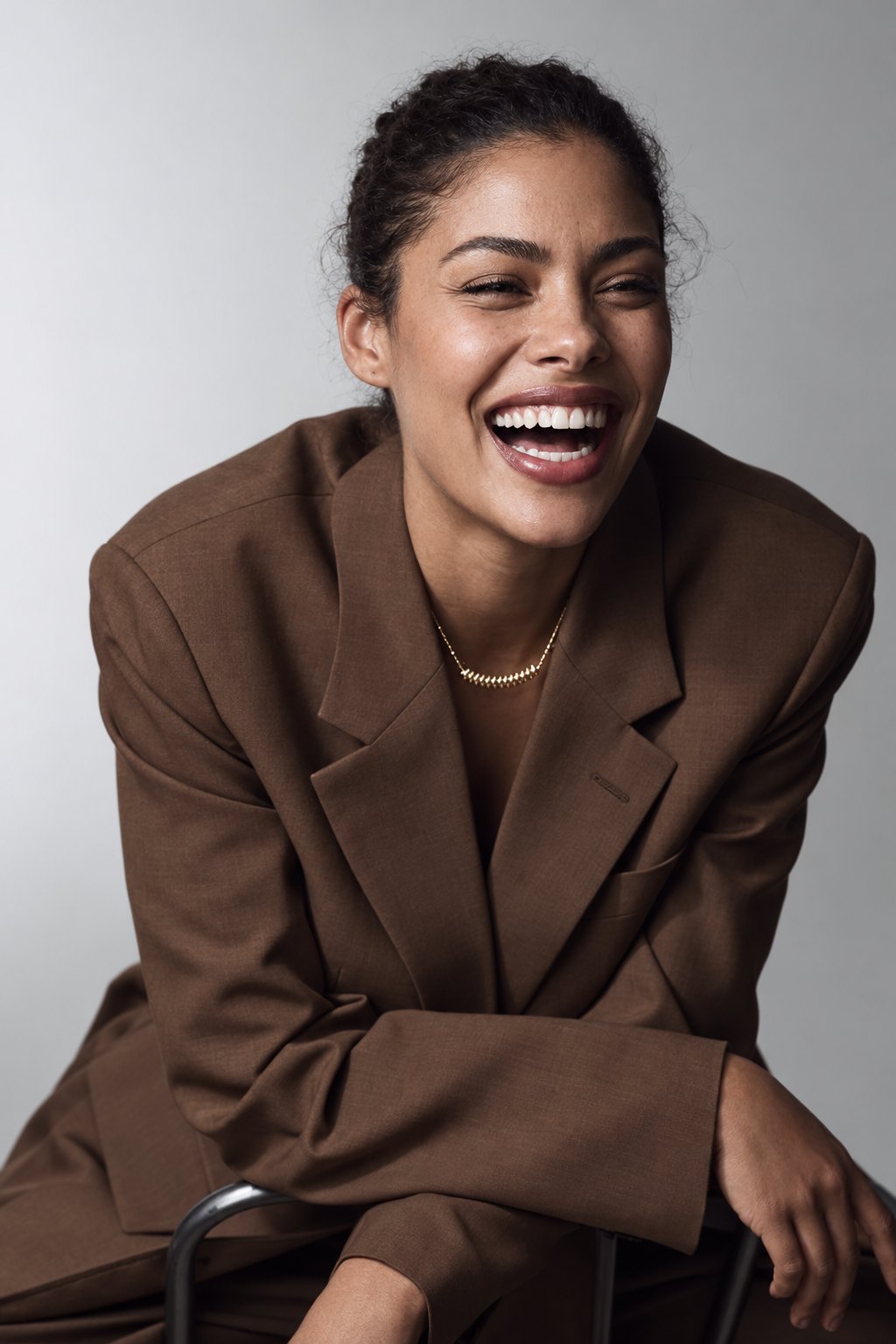 Young woman in a brown suit laughing, leaning on the back of a chair