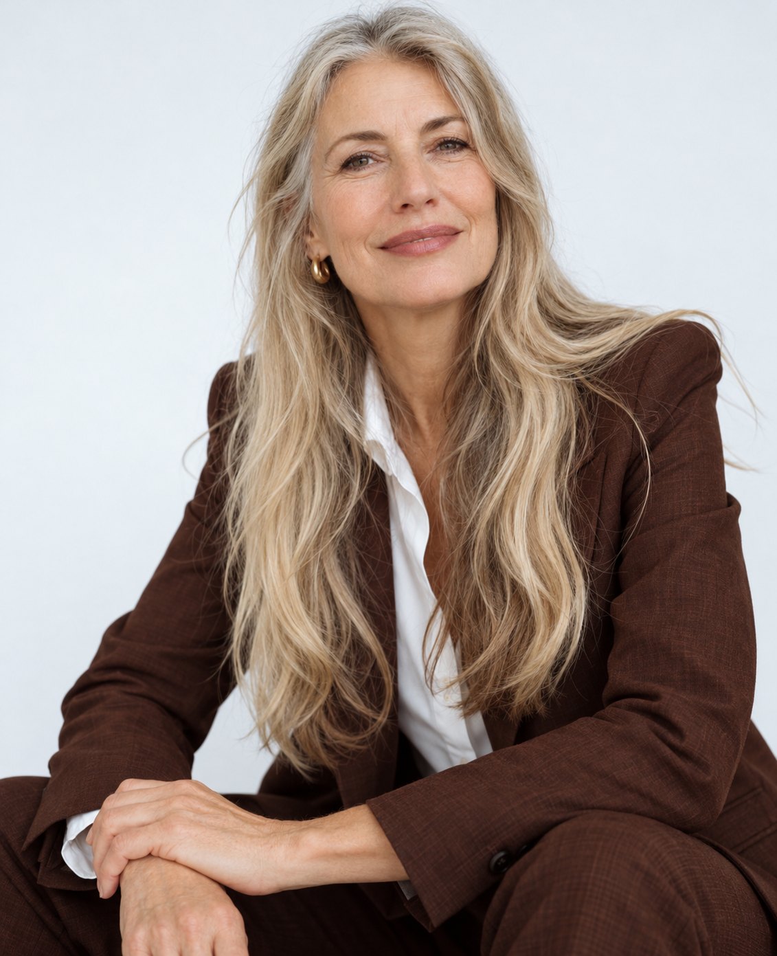 Senior woman with long grey-blonde hair in a brown suit, smiling